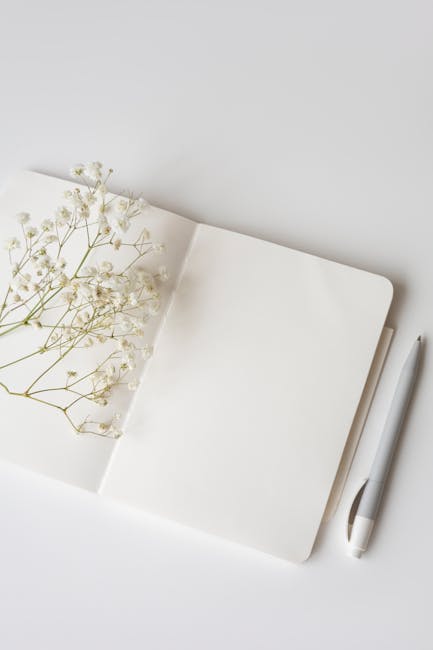 Open notepad with a pen and dried flowers on a white surface. Ideal for bloggers and stationery lovers.